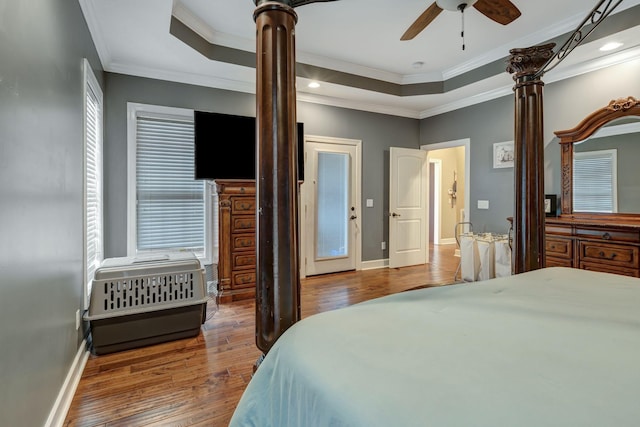 bedroom featuring ornate columns, hardwood / wood-style flooring, ornamental molding, ceiling fan, and a tray ceiling