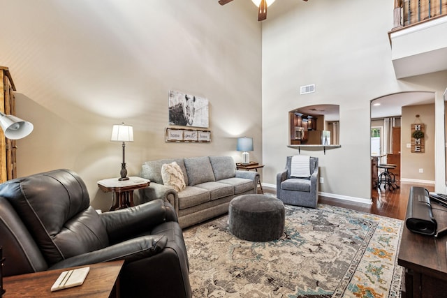 living room with ceiling fan, wood-type flooring, and a towering ceiling