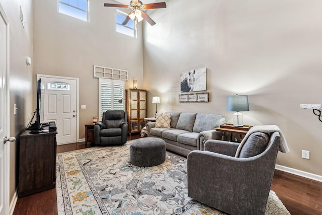 living room featuring dark wood-type flooring, ceiling fan, and a high ceiling