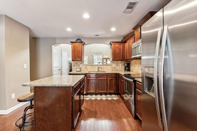 kitchen with appliances with stainless steel finishes, a center island, tasteful backsplash, a kitchen bar, and dark hardwood / wood-style flooring