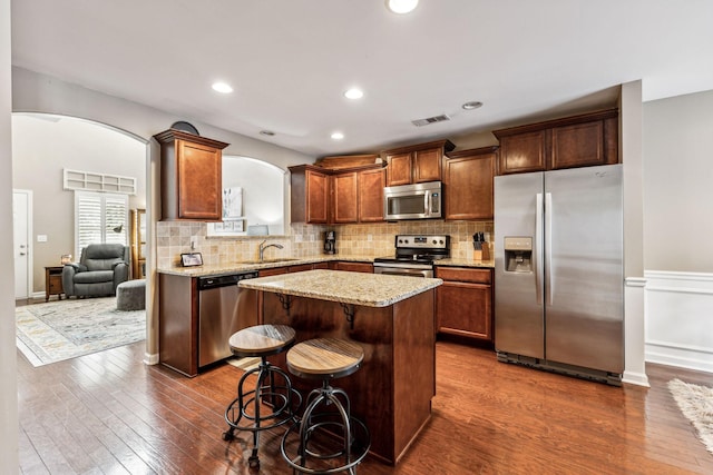 kitchen featuring dark wood-type flooring, a breakfast bar, sink, appliances with stainless steel finishes, and a kitchen island