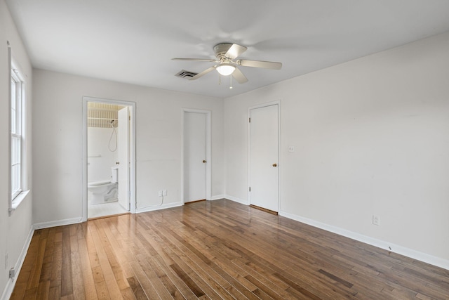 unfurnished bedroom featuring multiple windows, wood-type flooring, ensuite bathroom, and ceiling fan