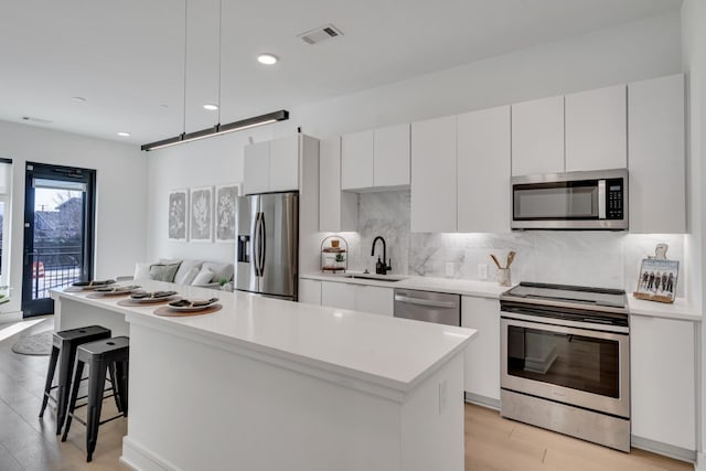 kitchen with white cabinetry, sink, backsplash, a center island, and stainless steel appliances