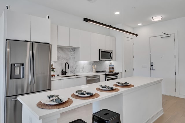 kitchen with appliances with stainless steel finishes, white cabinetry, sink, backsplash, and a center island