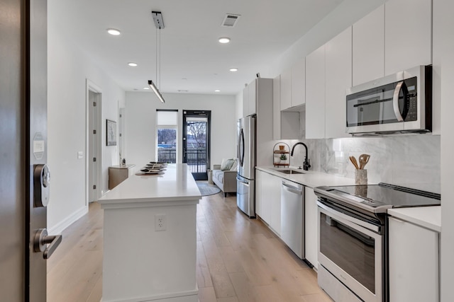 kitchen with sink, white cabinetry, tasteful backsplash, appliances with stainless steel finishes, and light hardwood / wood-style floors