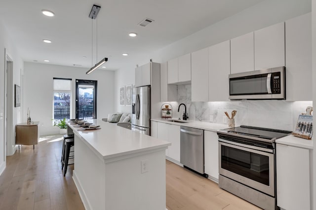 kitchen with sink, appliances with stainless steel finishes, white cabinetry, a center island, and decorative light fixtures