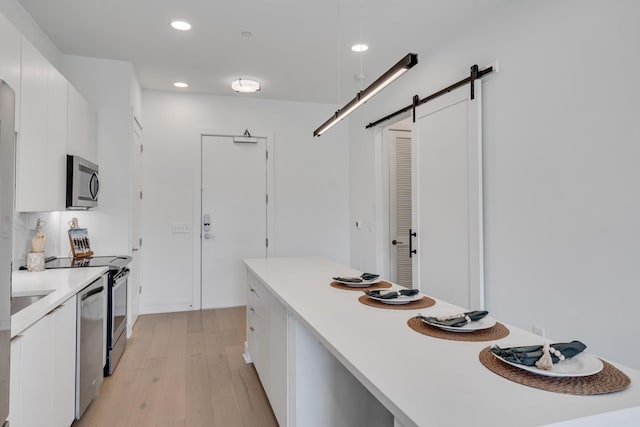 kitchen featuring light hardwood / wood-style floors, stainless steel appliances, a barn door, and white cabinets