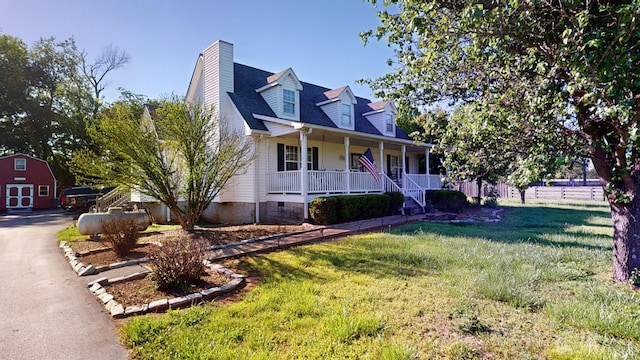 new england style home with an outbuilding, covered porch, and a front lawn