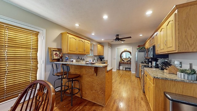 kitchen with a breakfast bar, kitchen peninsula, ceiling fan, stainless steel appliances, and light stone countertops