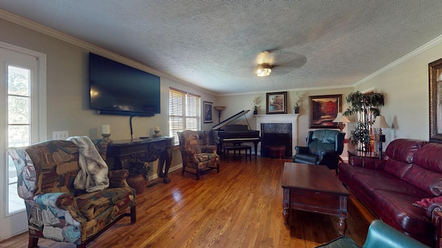 living room featuring a tile fireplace, hardwood / wood-style floors, a textured ceiling, and crown molding