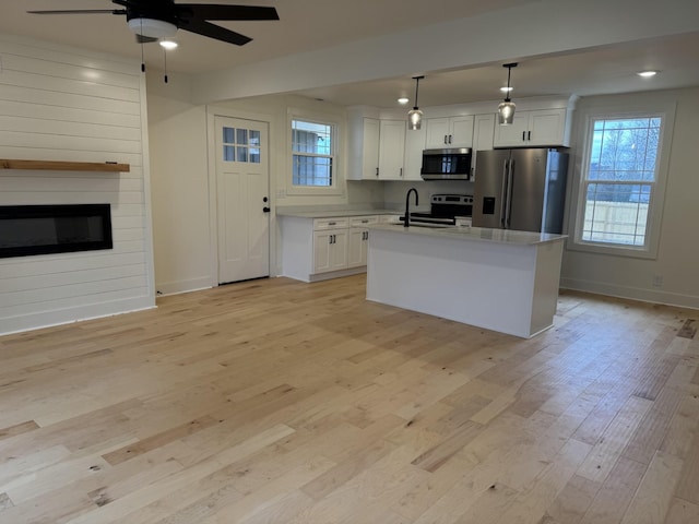 kitchen featuring pendant lighting, a kitchen island with sink, white cabinets, and appliances with stainless steel finishes