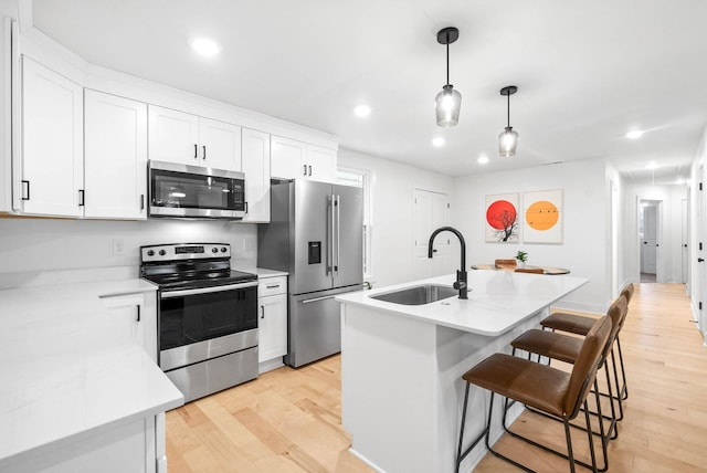 kitchen with sink, white cabinetry, hanging light fixtures, appliances with stainless steel finishes, and an island with sink