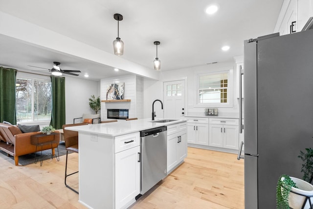 kitchen with sink, decorative light fixtures, appliances with stainless steel finishes, a kitchen island with sink, and white cabinets