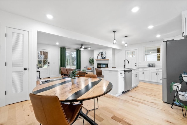 kitchen with appliances with stainless steel finishes, decorative light fixtures, white cabinetry, an island with sink, and sink