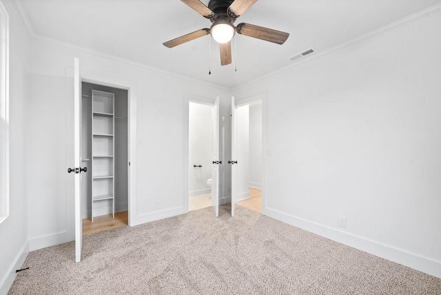 unfurnished bedroom featuring crown molding, light colored carpet, a closet, and a spacious closet