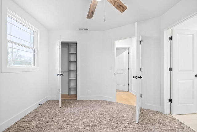 unfurnished bedroom with a walk in closet, light carpet, ceiling fan, and a closet