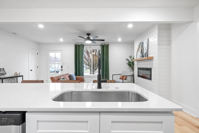 kitchen featuring sink, light stone counters, a large fireplace, white cabinets, and stainless steel dishwasher