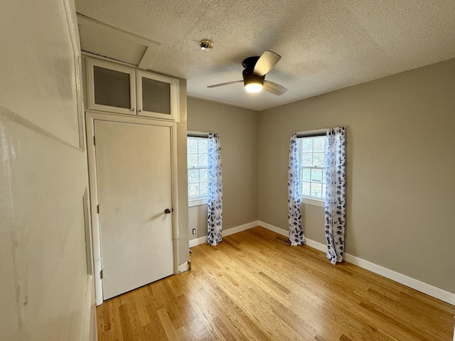 unfurnished bedroom featuring baseboards, ceiling fan, a textured ceiling, and light wood-style floors