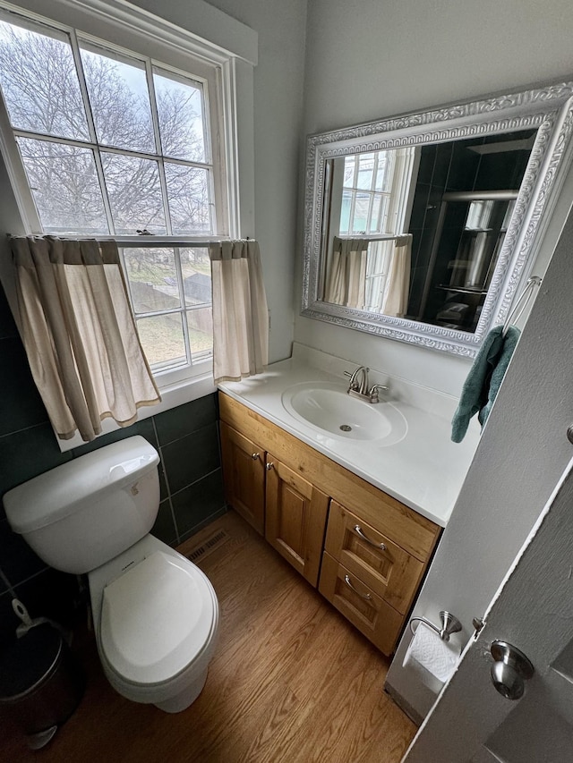 bathroom featuring a shower, toilet, wood finished floors, vanity, and tile walls