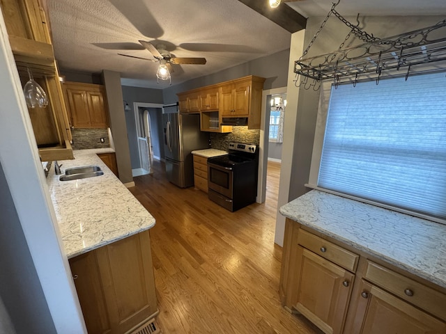 kitchen with light stone counters, stainless steel appliances, a sink, light wood-type flooring, and backsplash