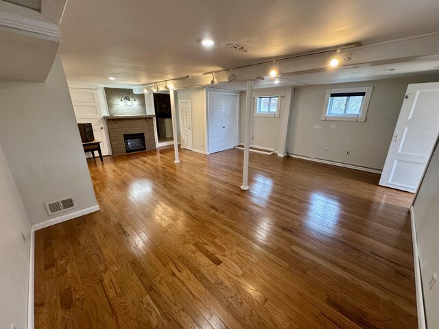 unfurnished living room featuring a glass covered fireplace, wood finished floors, visible vents, and baseboards