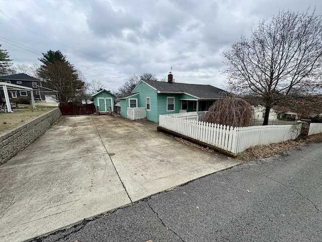 view of front of house featuring a storage shed, concrete driveway, a fenced front yard, a chimney, and an outdoor structure