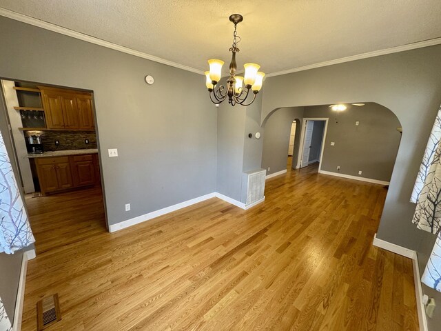 unfurnished dining area with arched walkways, light wood-style flooring, visible vents, baseboards, and an inviting chandelier