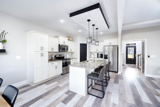 kitchen featuring sink, appliances with stainless steel finishes, white cabinetry, light stone countertops, and a center island with sink