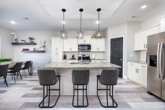 kitchen featuring white cabinetry, appliances with stainless steel finishes, a kitchen island with sink, and decorative light fixtures