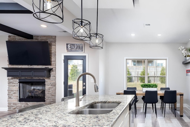 kitchen featuring plenty of natural light, sink, white cabinets, hanging light fixtures, and light stone countertops