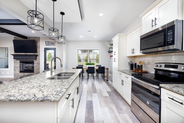 kitchen featuring pendant lighting, sink, appliances with stainless steel finishes, white cabinetry, and a center island with sink