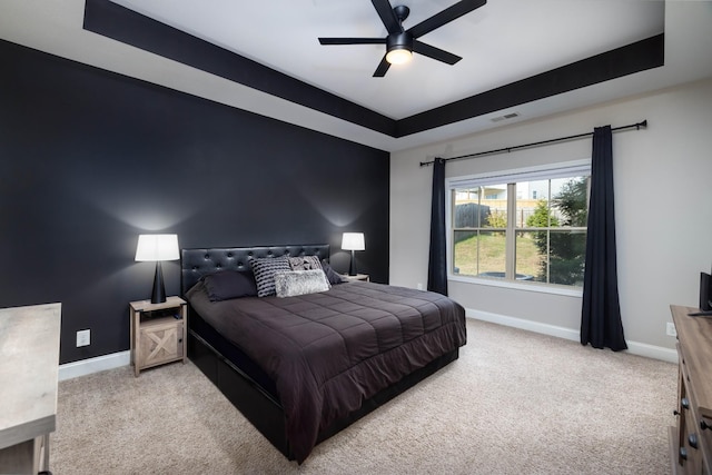 carpeted bedroom with a raised ceiling and ceiling fan