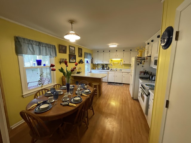 kitchen with white appliances, light hardwood / wood-style flooring, white cabinetry, hanging light fixtures, and kitchen peninsula