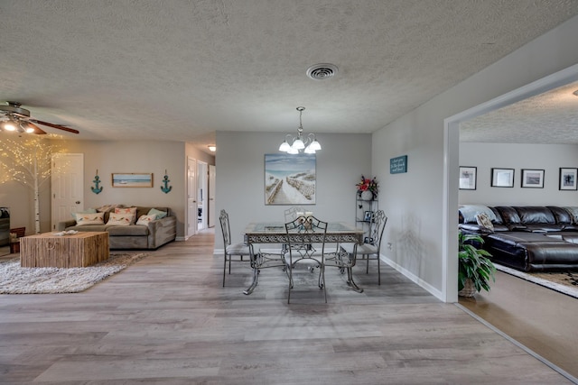 dining room featuring ceiling fan with notable chandelier, a textured ceiling, and light hardwood / wood-style flooring