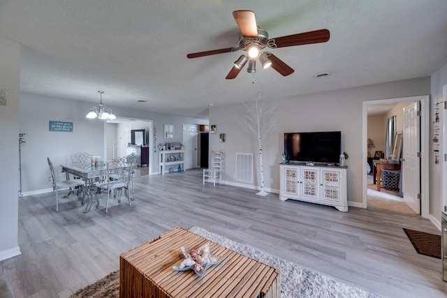 living room featuring hardwood / wood-style flooring, ceiling fan with notable chandelier, and a textured ceiling