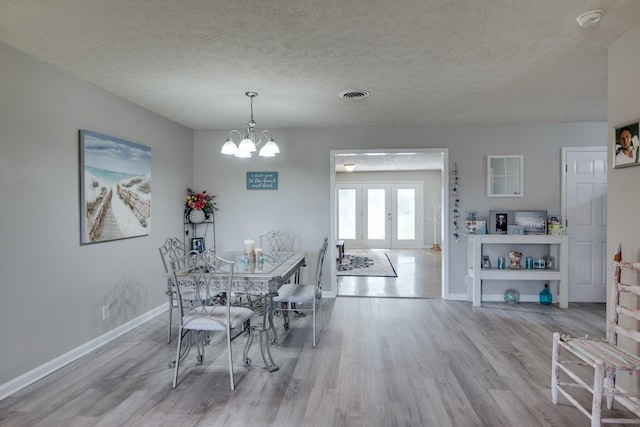 unfurnished dining area with french doors, a notable chandelier, a textured ceiling, and light wood-type flooring