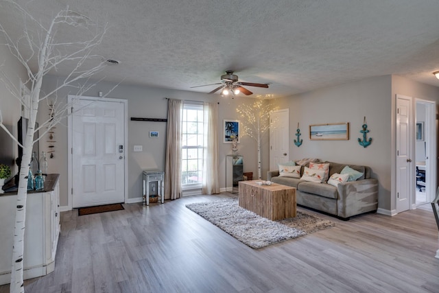 living room with ceiling fan, a textured ceiling, and light wood-type flooring