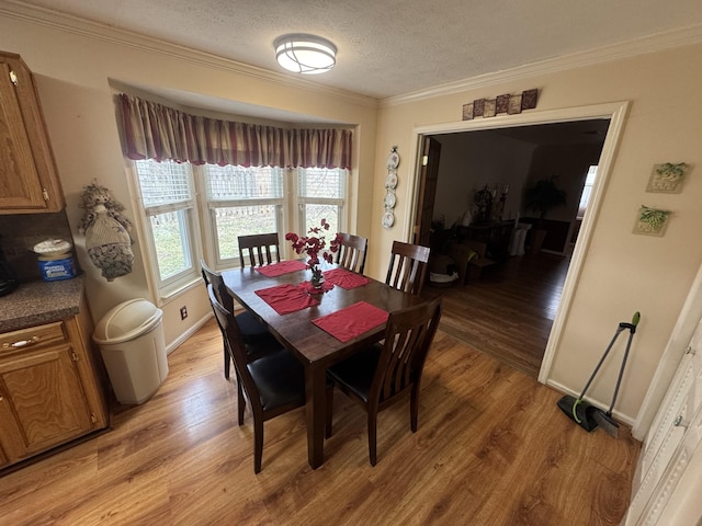 dining area with ornamental molding, a textured ceiling, and light hardwood / wood-style flooring