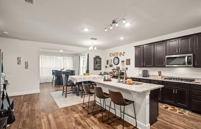 kitchen with appliances with stainless steel finishes, dark hardwood / wood-style floors, sink, a kitchen breakfast bar, and a kitchen island with sink