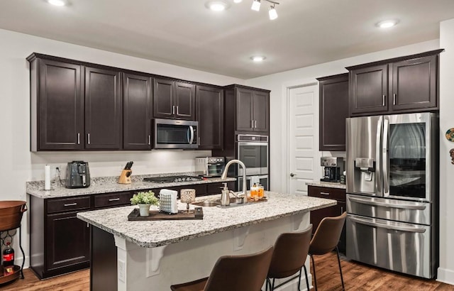 kitchen with appliances with stainless steel finishes, an island with sink, sink, a kitchen bar, and light stone counters