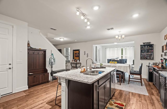 kitchen with a kitchen island with sink, sink, light stone counters, and light wood-type flooring