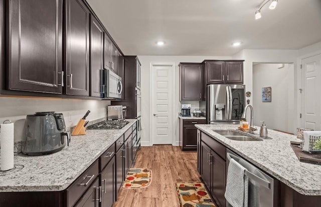 kitchen with sink, appliances with stainless steel finishes, a kitchen island with sink, dark brown cabinetry, and light hardwood / wood-style floors