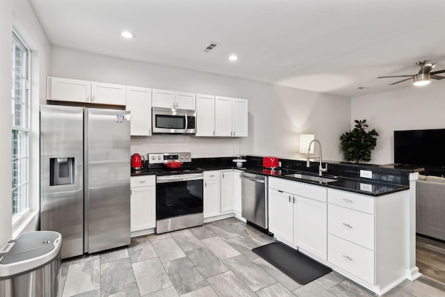 kitchen featuring sink, appliances with stainless steel finishes, backsplash, white cabinets, and kitchen peninsula