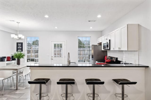 kitchen with tasteful backsplash, a breakfast bar area, white cabinets, hanging light fixtures, and stainless steel appliances