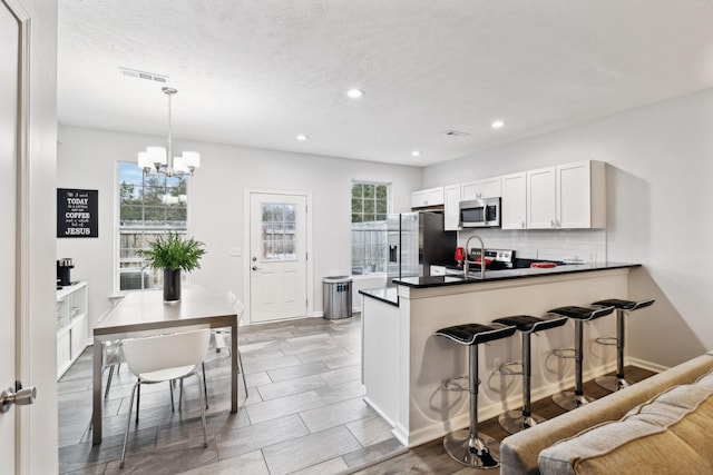 kitchen featuring pendant lighting, white cabinets, decorative backsplash, kitchen peninsula, and stainless steel appliances