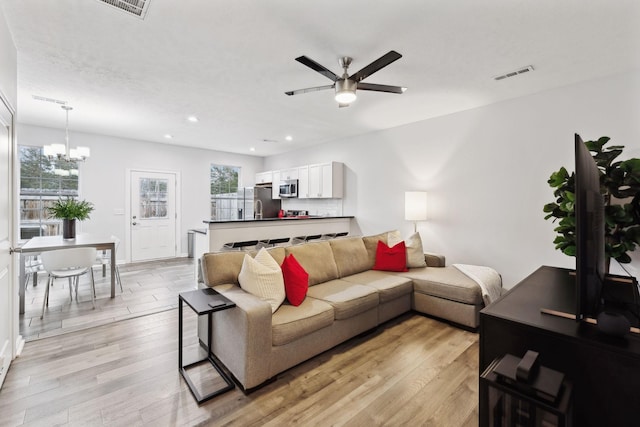 living room with ceiling fan with notable chandelier and light hardwood / wood-style flooring