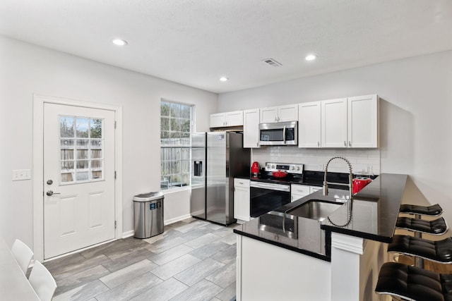 kitchen with appliances with stainless steel finishes, sink, white cabinets, backsplash, and kitchen peninsula