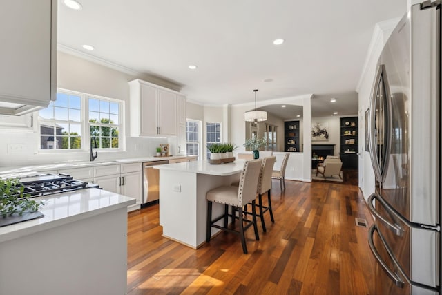 kitchen featuring white cabinetry, crown molding, decorative light fixtures, a center island, and appliances with stainless steel finishes