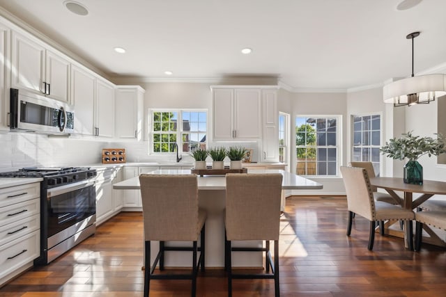 kitchen featuring pendant lighting, white cabinetry, backsplash, stainless steel appliances, and a kitchen island