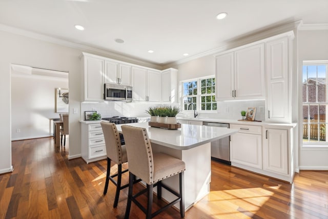 kitchen with white cabinetry, stainless steel appliances, ornamental molding, a kitchen island, and dark hardwood / wood-style flooring